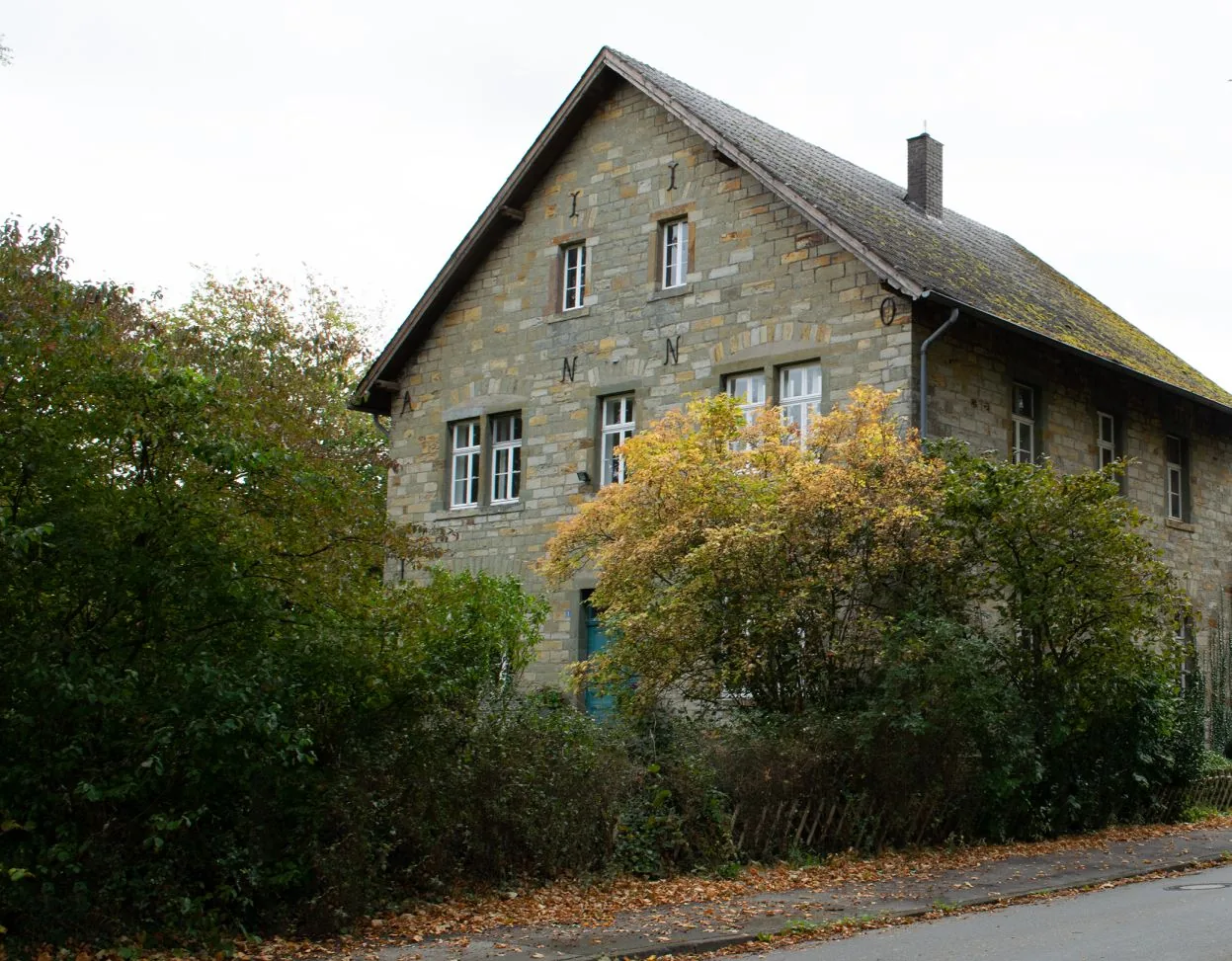 Das alte Forsthaus: Bruchsteinhaus mit steilem Giebel, davor herbstliche Sträucher